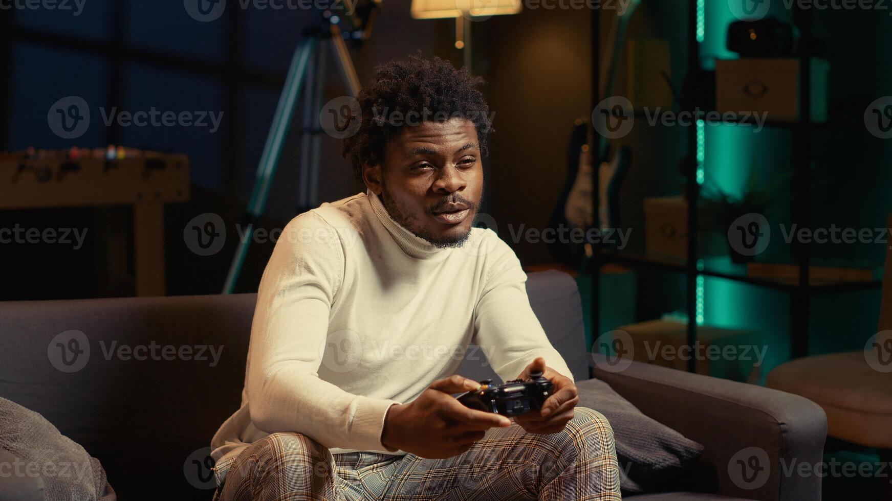 African american man sitting on couch at home, relaxing by playing videogames on gaming console. Gamer unwinding in apartment by competing in online multiplayer tournament photo