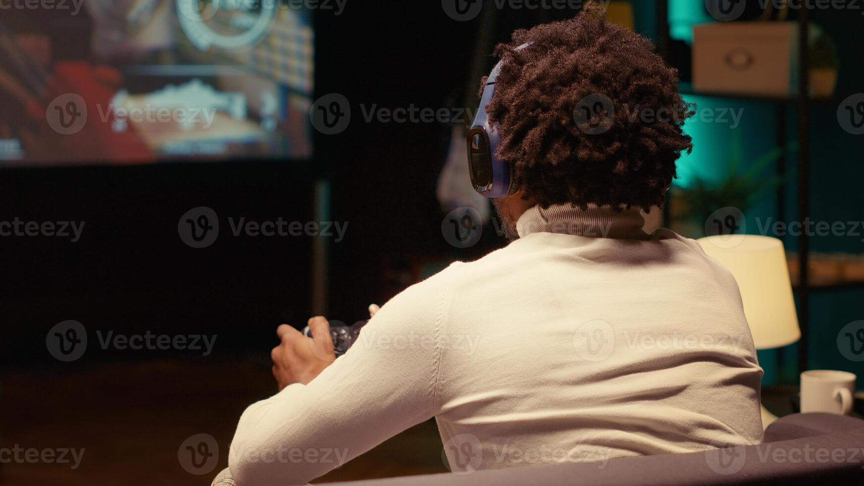 Close up shot of BIPOC man playing SF FPS videogame on widescreen smart TV, having fun in dark apartment room. Gamer competing in online multiplayer game, using headphones to chat with teammates photo