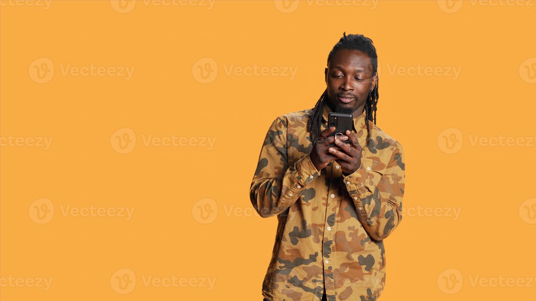 African american guy navigating on social media app, using smartphone to check online websites in studio. Male model browsing internet pages on phone network, smiling on camera. photo