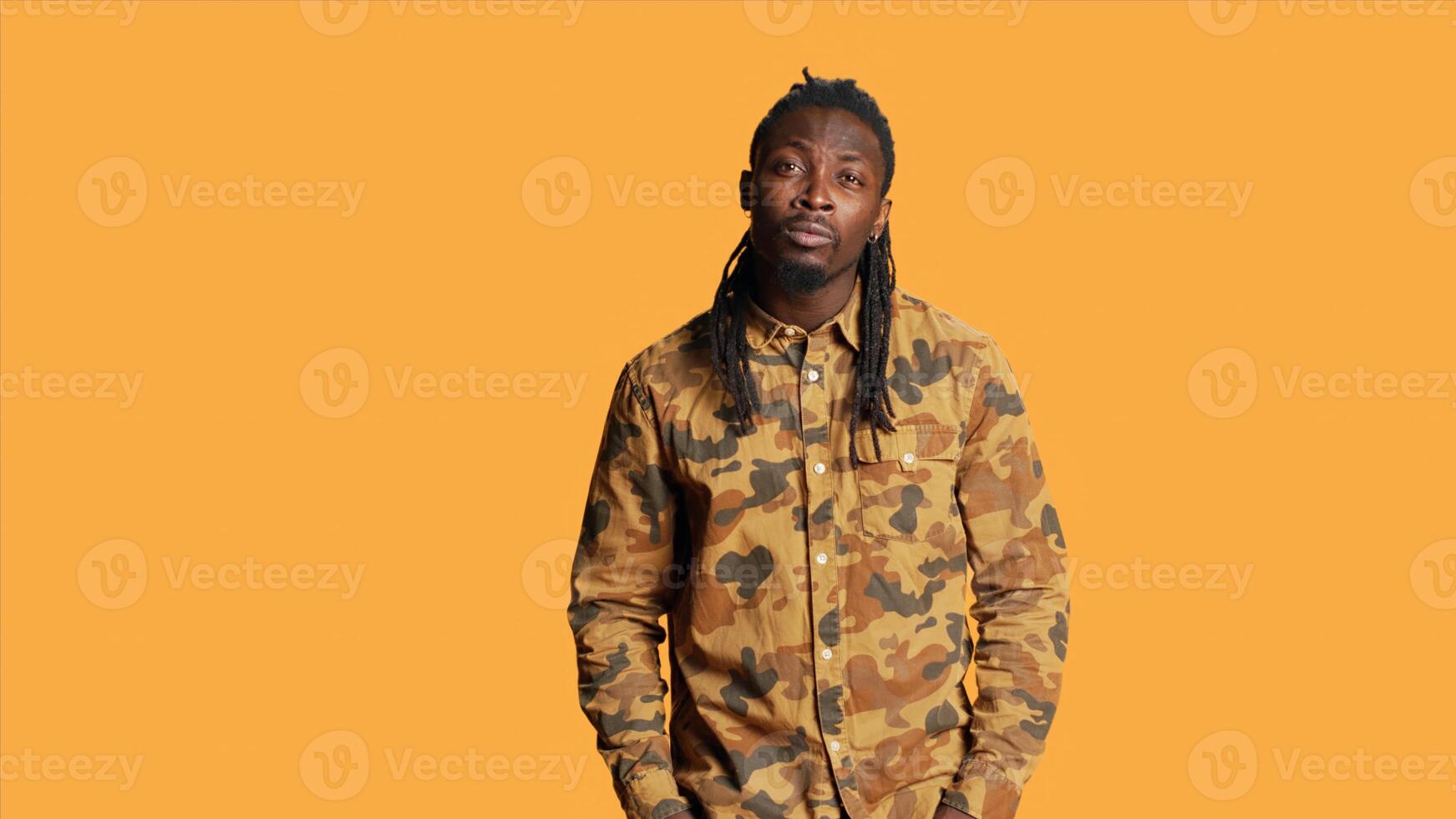 Shocked african american man saying wow on camera feeling amazed by something in front of him. Surprised excited person with dreads smiling in studio over orange background. photo