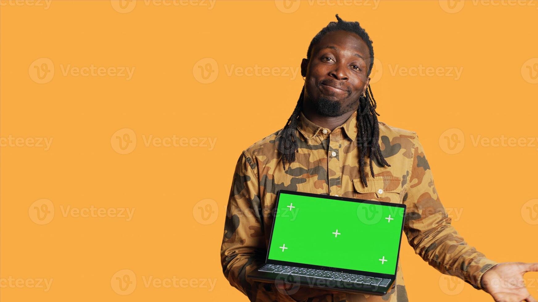 Young guy showing pc with greenscreen layout on camera, pointing at isolated chromakey display. African american man presenting laptop with blank copyspace mockup screen in studio. photo