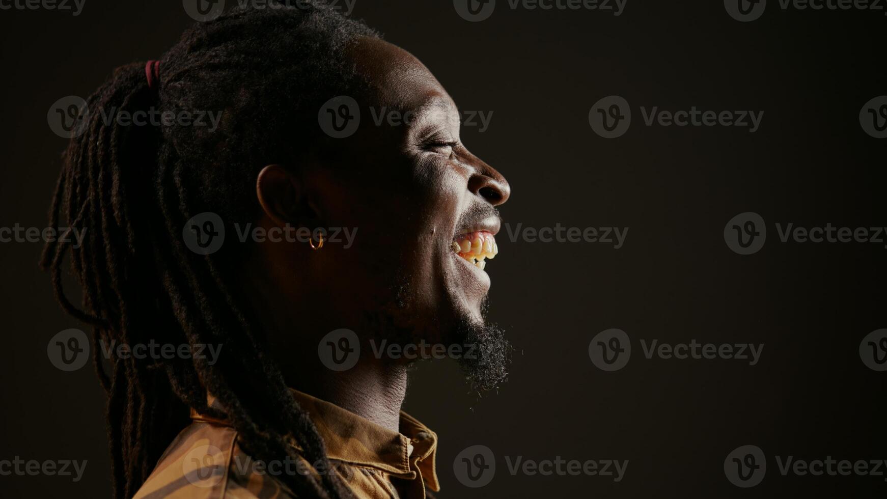 African american guy having fun on black background, laughing at jokes with his colleagues and enjoying free leisure time at the studio. Adult feeling joyful, laughs at funny memes. Handheld shot. photo