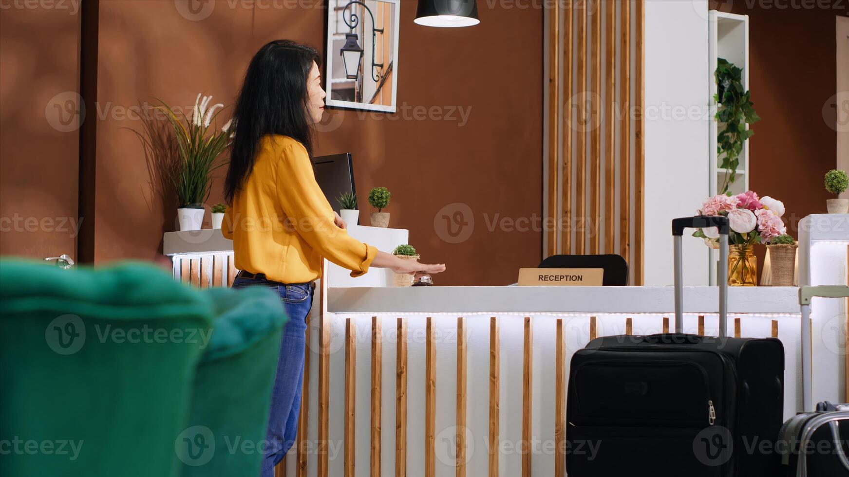 Asian guest arriving at front desk and ringing service bell to receive assistance for accommodation, calling for receptionist to do check in process. Woman talking to hotel staff. Handheld shot. photo