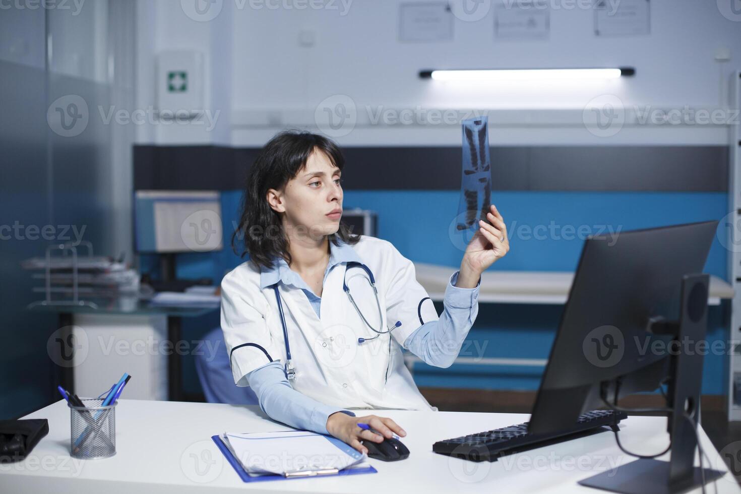 Dedicated doctor examining a CT scan of a patient, taking notes on desktop computer. The image shows caucasian female healthcare professional inspecting a chest X-ray image of an individual. photo