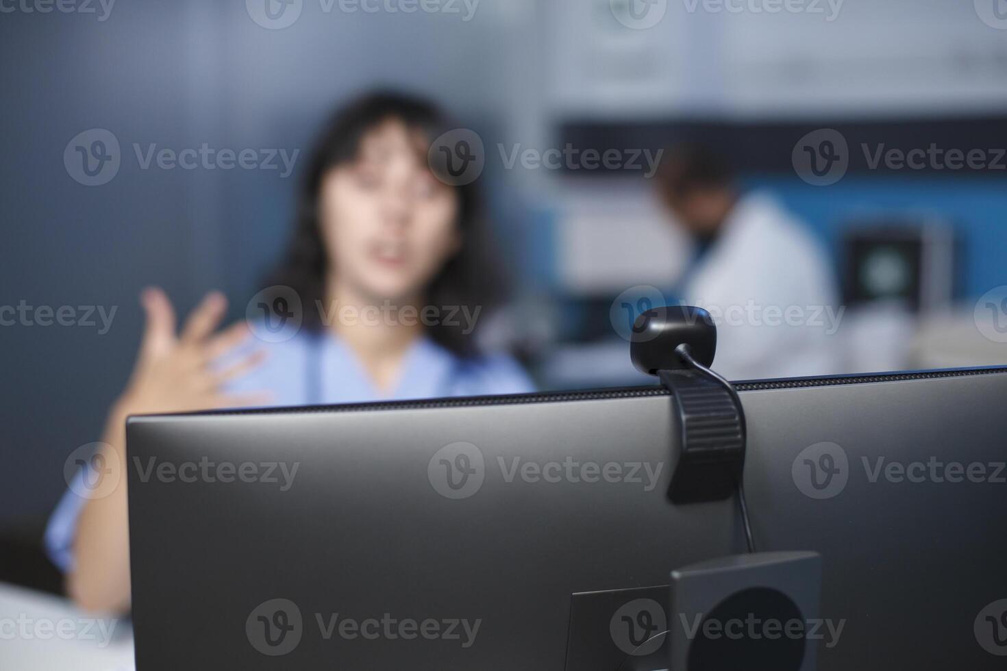 Selective focus on computer being used by nurse practitioner at a hospital for a video call. Caucasian woman is seated in the clinic office, participating in a virtual conference. Close-up shot. photo