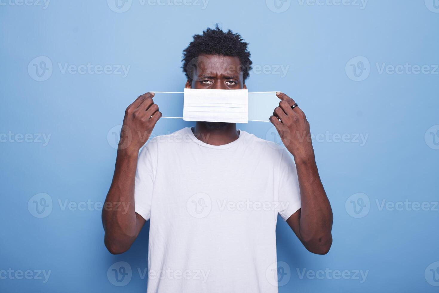 Portrait of black guy putting on face mask to protect himself from coronavirus epidemic. African American adult staring at camera is wearing a mask for healthcare and preventative purposes. photo