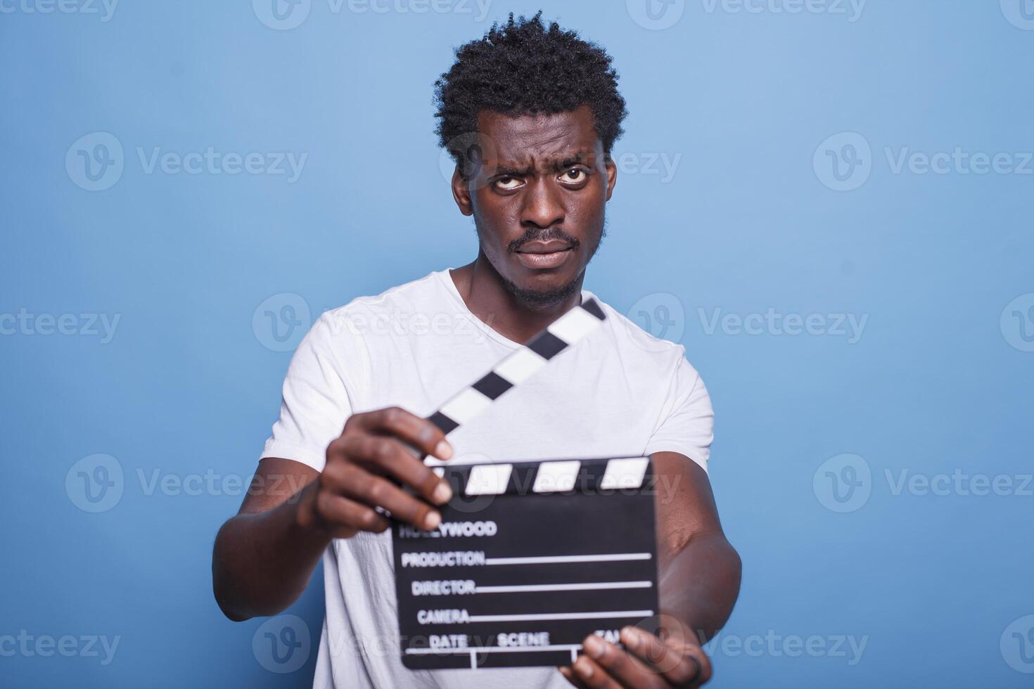 africano americano productor avaro un claqueta usado para corte escenas mientras mirando a cámara. retrato de negro chico utilizando un película badajo para película producción y cinematografía. foto