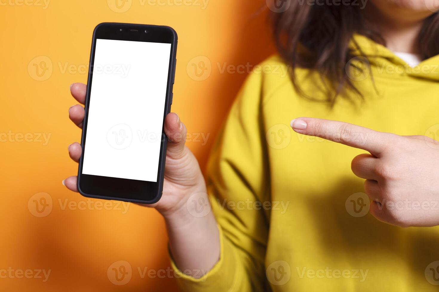 Photo focus on caucasian hand vertically grasping mobile device showing isolated mockup template in studio. Close-up of female individual holding and pointing to cell phone with white screen display.
