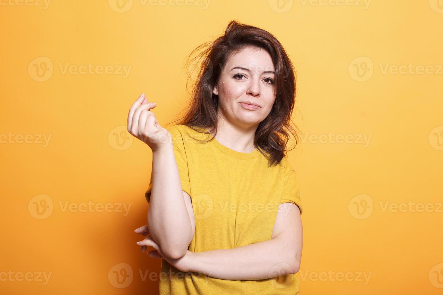 Confident female adult with brunette hair and a happy smile. She stands, looking at the camera, wearing casual clothing. Isolated orange background adds vibrancy to this cheerful portrait. photo