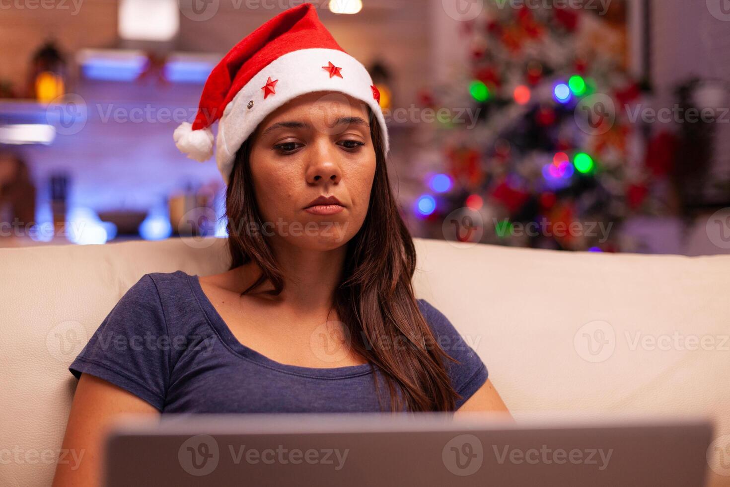 Woman looking at laptop screen reading business email during christmas holiday resting comfortable on couch in xmas decorated kitchen. Caucasian female browsing on social media. Winter season photo