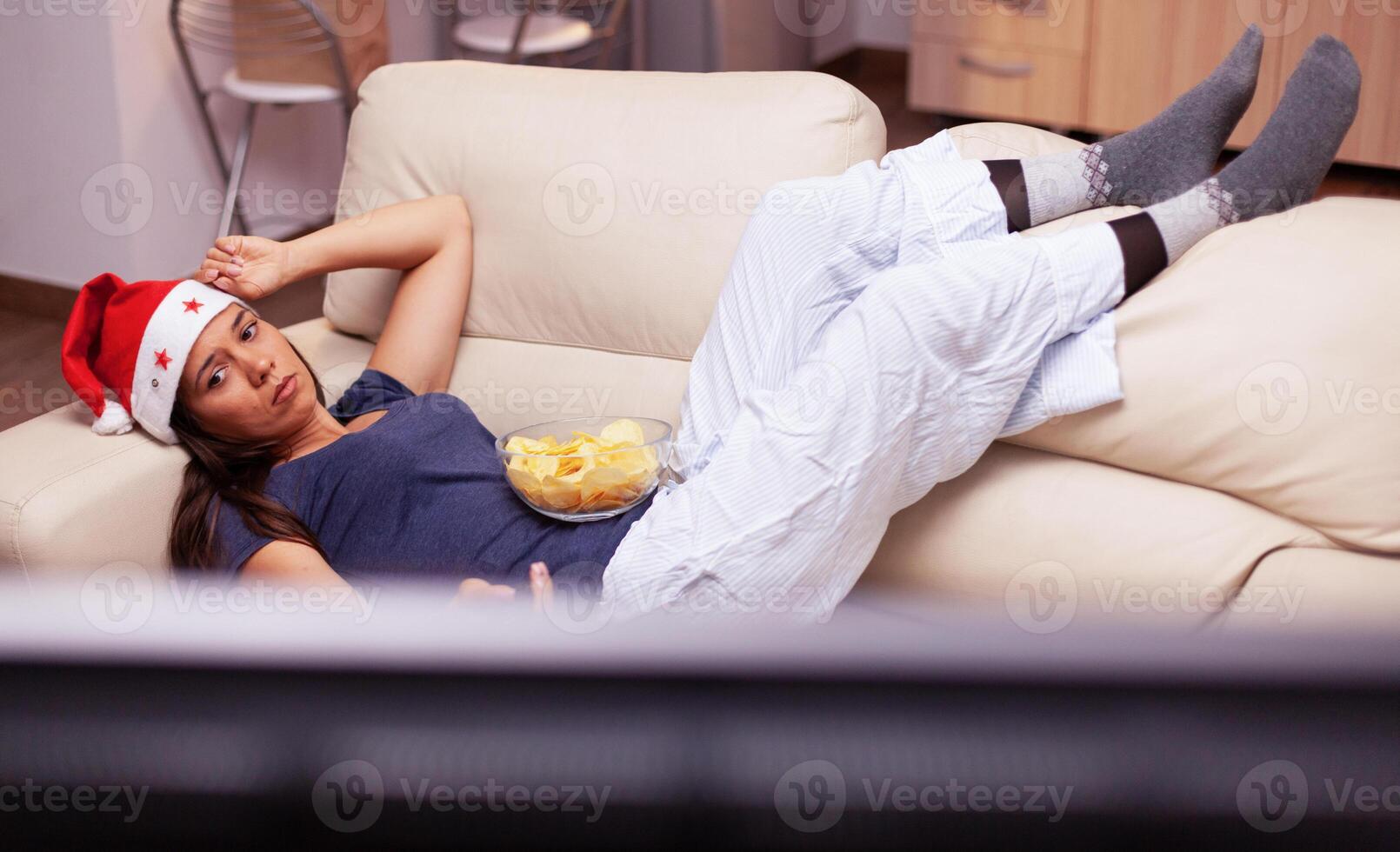 Adult person relaxing on sofa changing channel using remote searching xmas movie on television during christmastime. Woman enjoying winter holiday celebrating christmas season at home photo