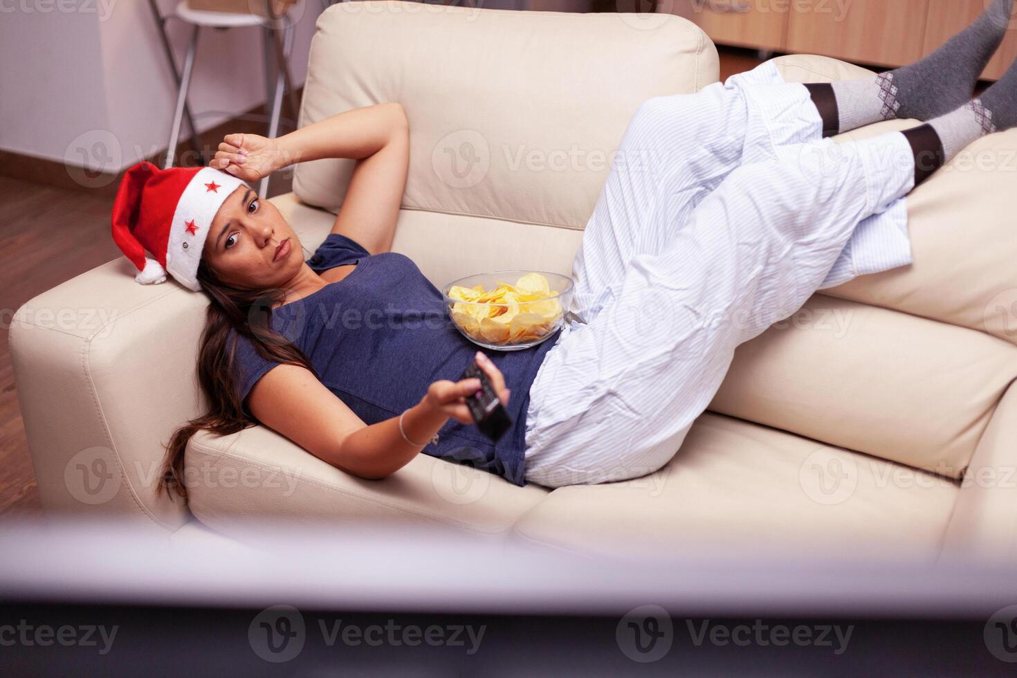 Adult person relaxing on couch changing channel using remote searching xmas fuuny movie on television during christmastime. Woman enjoying winter holiday celebrating christmas season at home photo