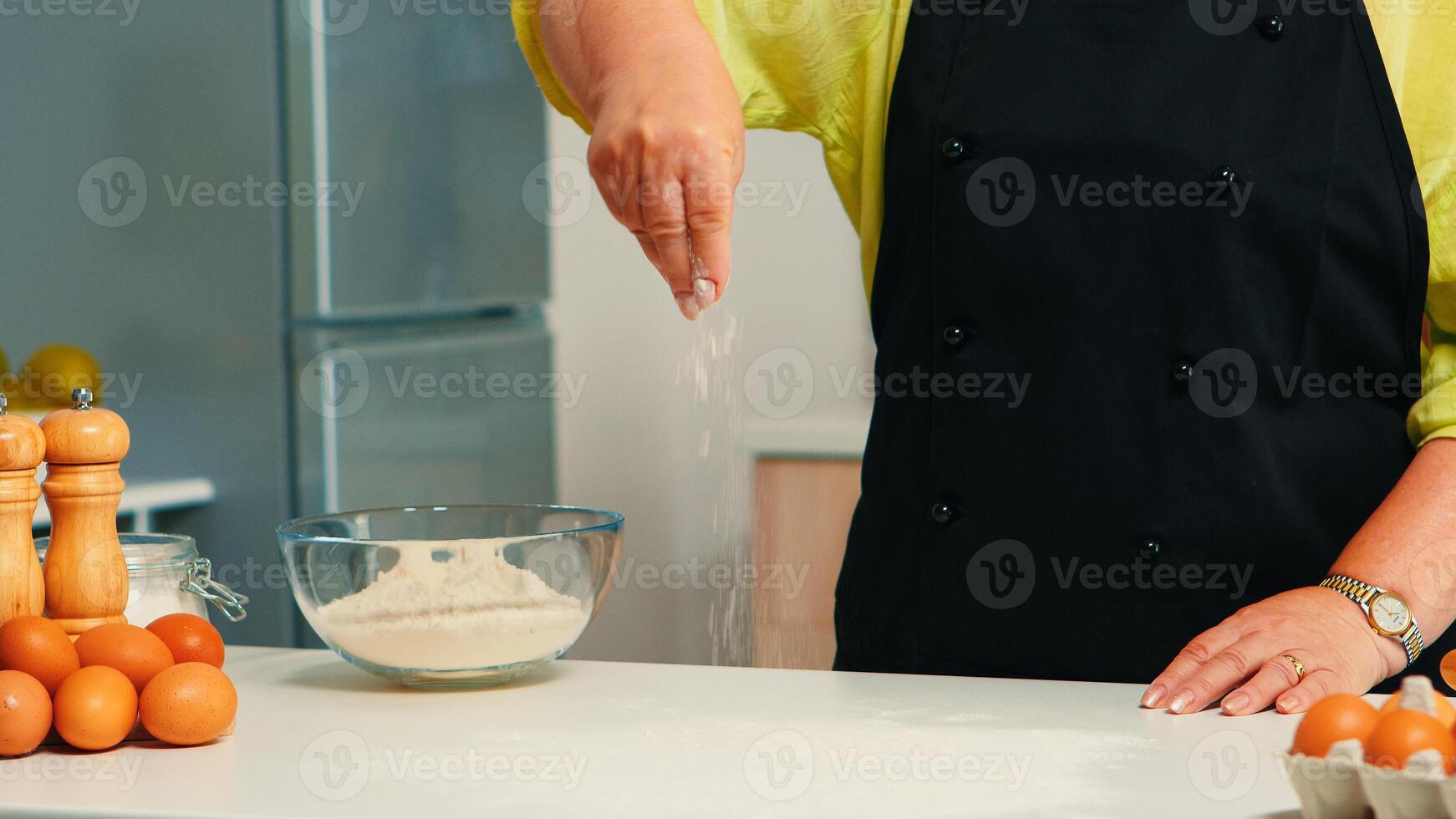 Close up of spreading flour in home kitchen for bakery products. Retired elderly chef with uniform sprinkling, sieving sifting raw ingredients by hand on wooden table baking homemade pizza, bread photo