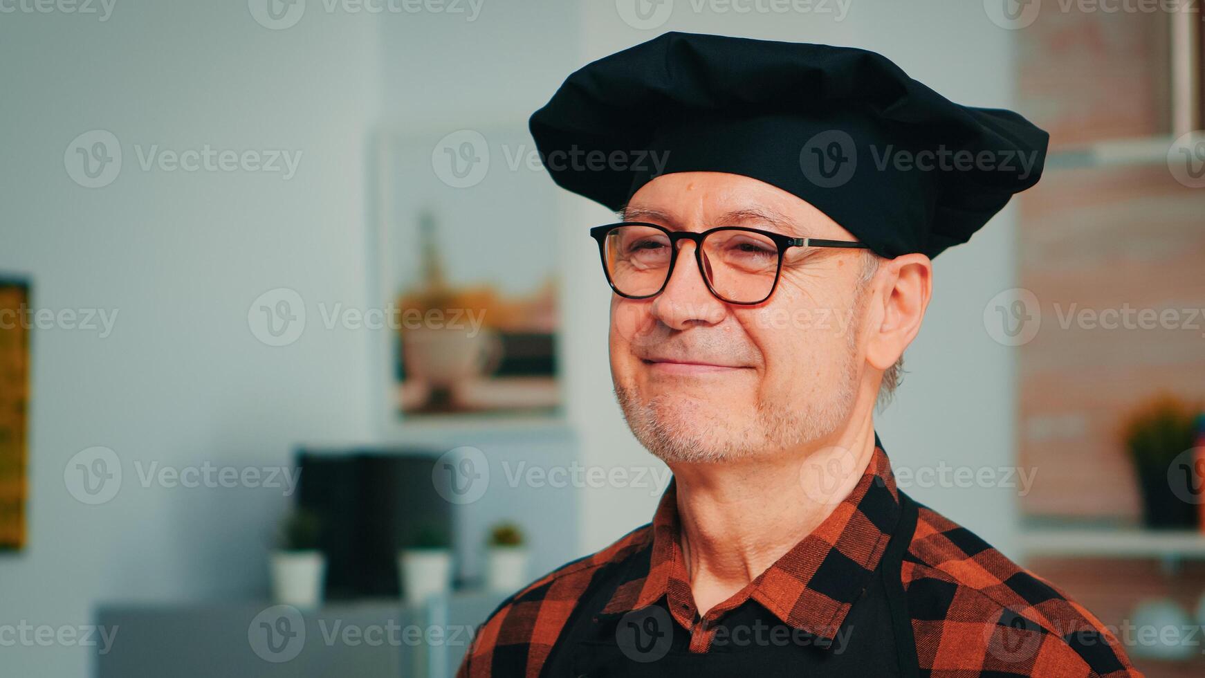 Elderly age man wearing chef bonete smiling in home kitchen. Close up portrait of happy retired old baker with glasses and apron looking at camera ready to cook homemade pastry with flour and eggs. photo