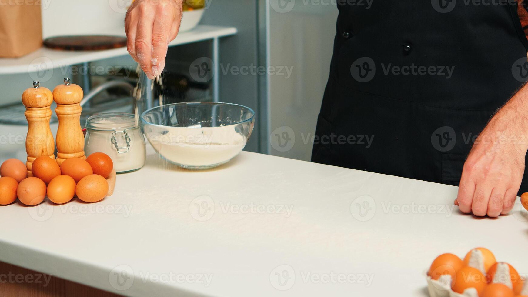 Baker spreading cookies ingredient on kitchen table top. Retired senior chef with bonete and apron, in kitchen uniform sprinkling sieving sifting ingredients by hand baking homemade pizza and bread photo