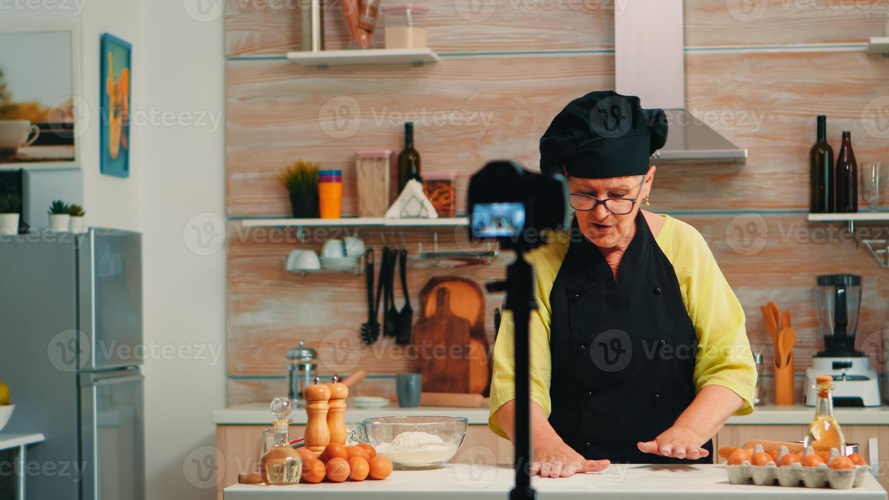 Senior baker speaking about flour while recording video tutorial. Retired blogger chef influencer using internet technology communicating, shooting, blogging on social media with digital equipment photo