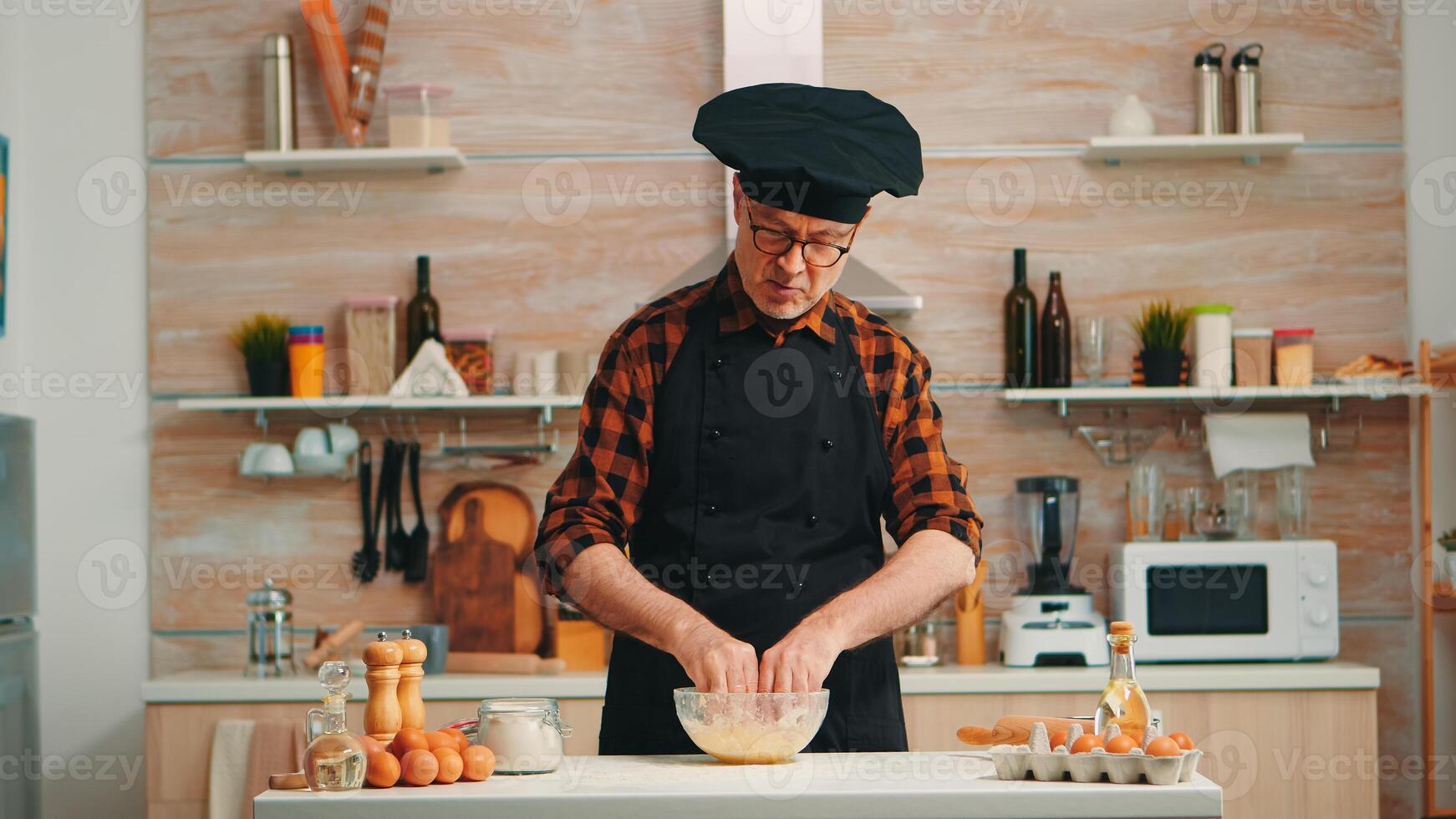 Baker man using flour for tasty traditional recipe in home kitchen speaking at camera. Retired blogger chef influencer using internet technology communicating on social media with digital equipment photo