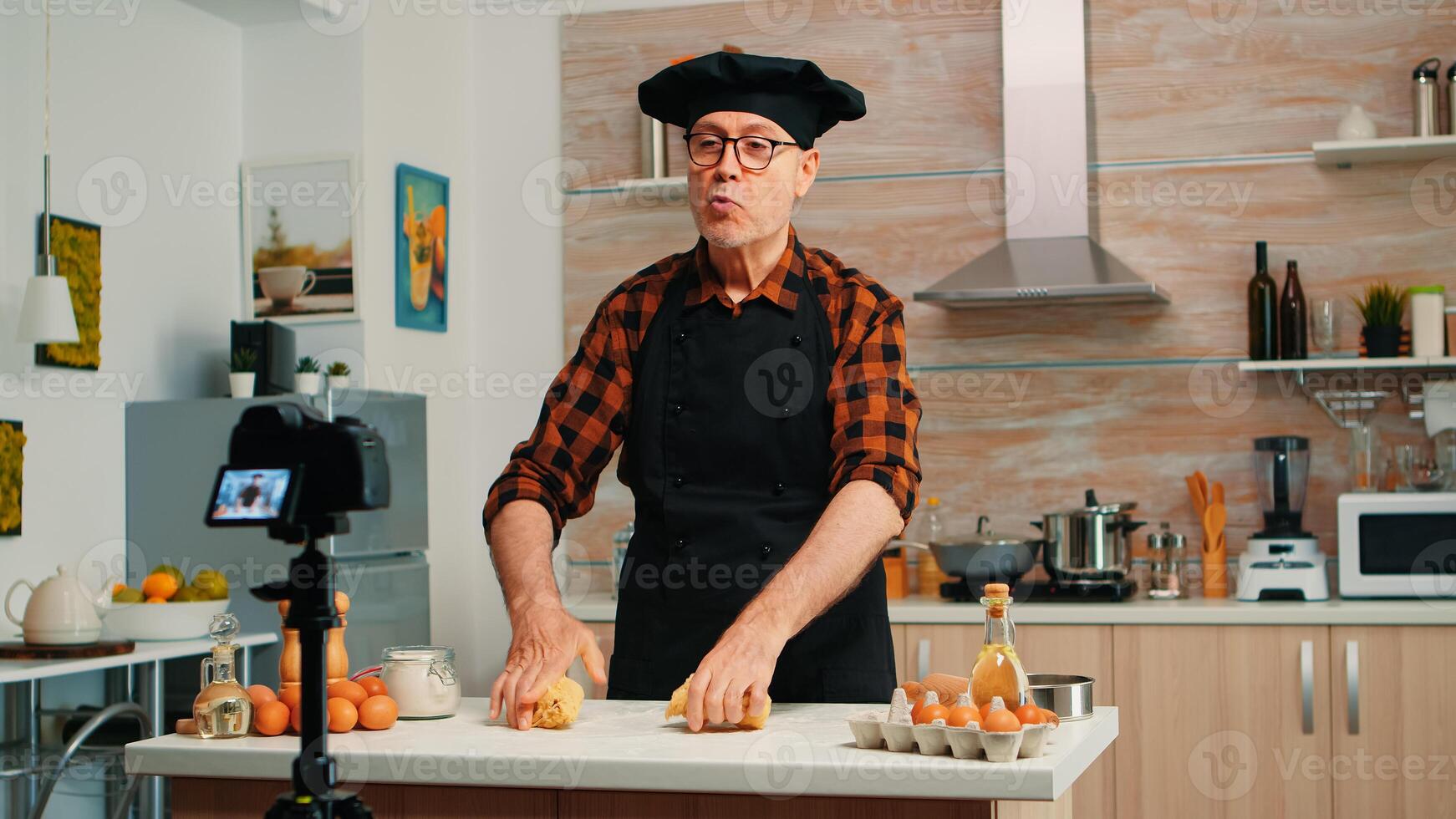 Grandfather recording food video in kitchen, preparing homemade pizza. Retired blogger chef influencer using internet technology communicating, shooting blogging on social media with digital equipment photo