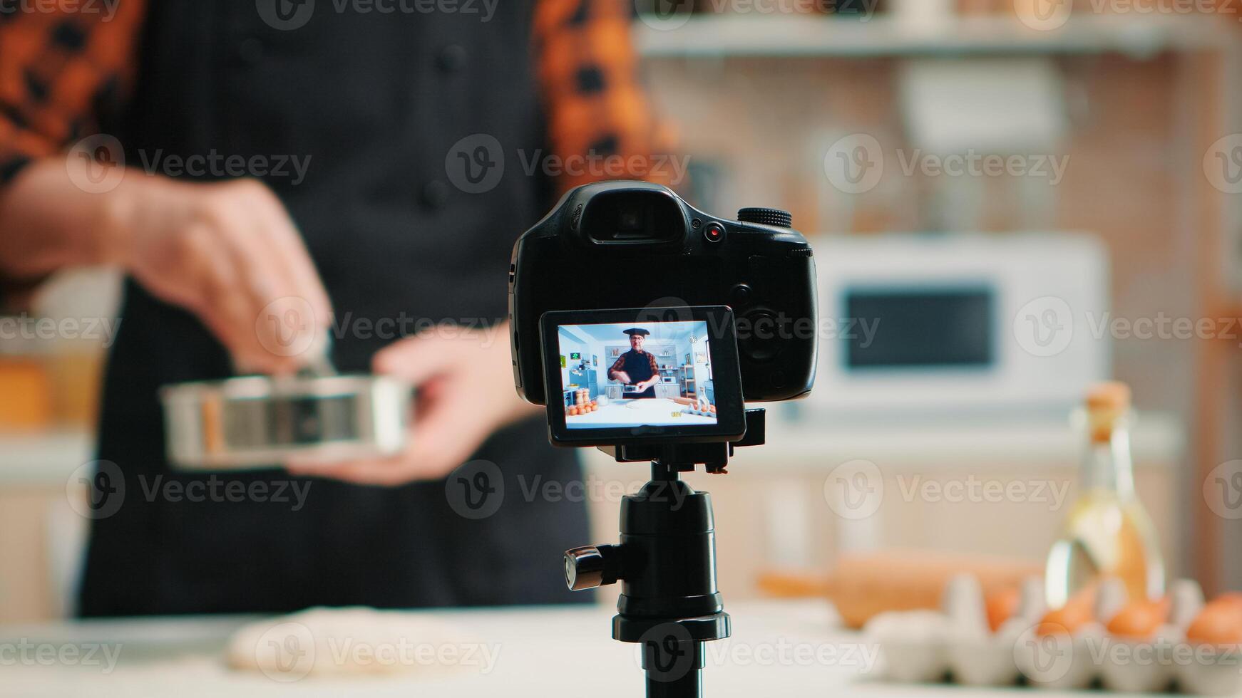 Close up of a video camera filming senior smiling man blogger in kitchen cooking. Retired blogger chef influencer using internet technology communicating on social media with digital equipment photo