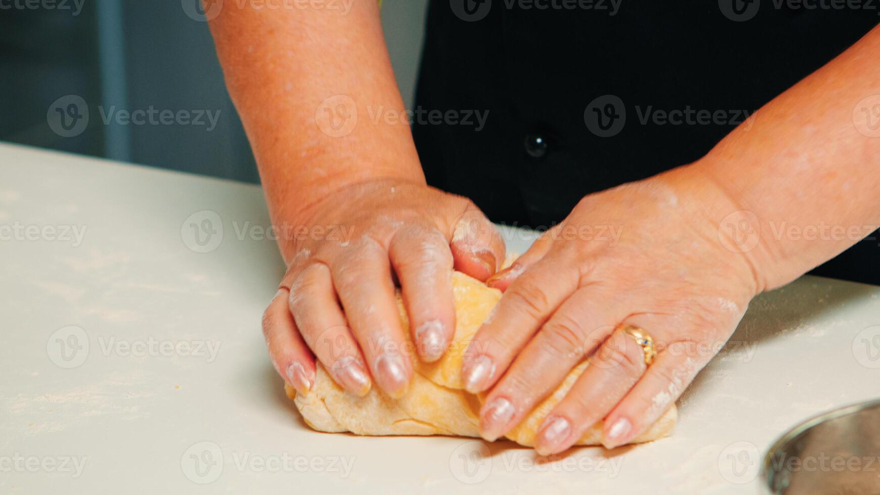 Close up of hands taking a large piece of pastry, making buns from dough. Retired elderly baker with bonete mixing ingredients with sifted wheat flour kneading for baking traditional cake and bread. photo