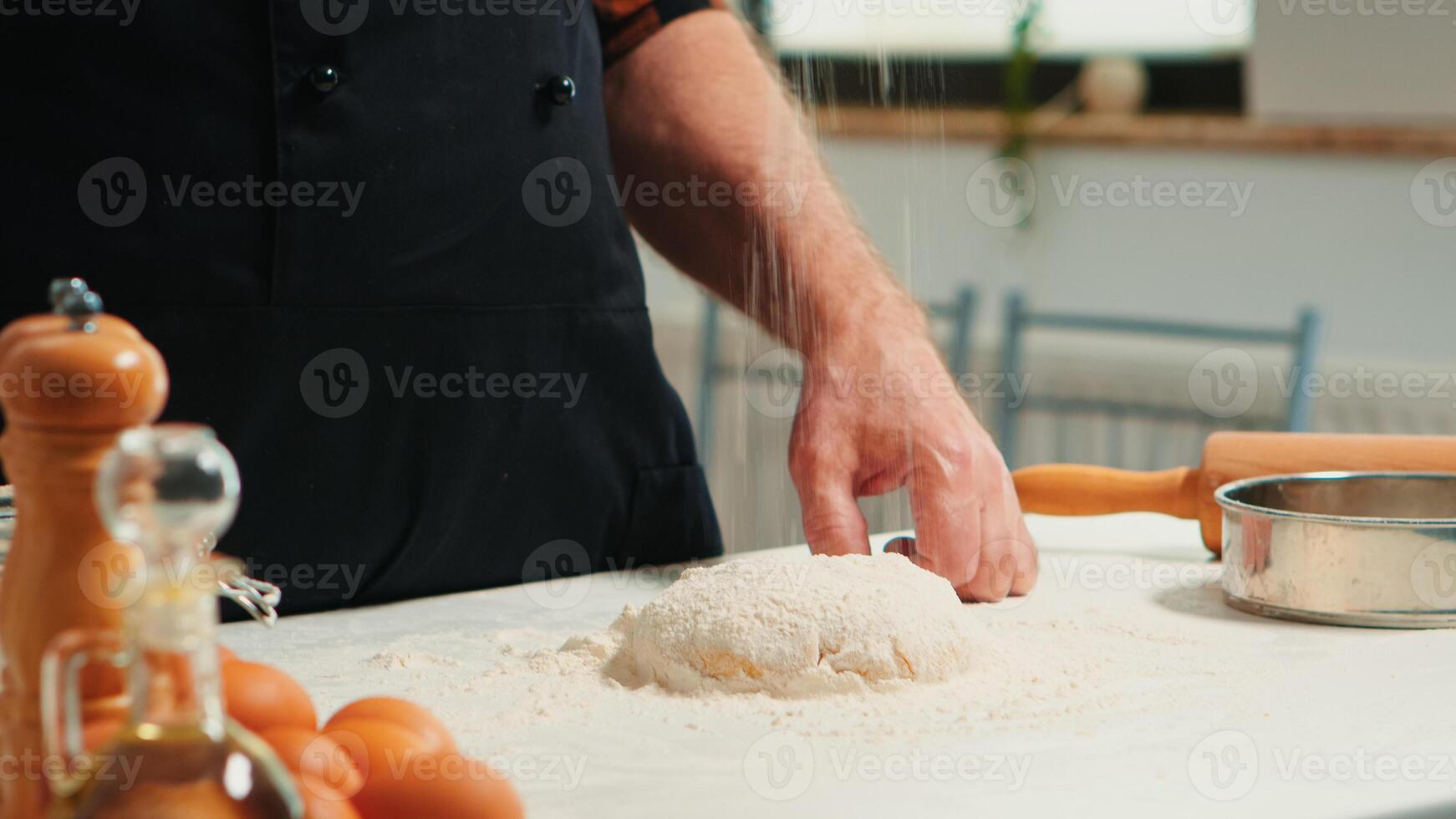 Baker adding flour on the pile by hand preparing bread dough. Close up of retired elderly chef with bonete and uniform sprinkling, sieving spreading rew ingredients baking homemade pizza and cackes. photo