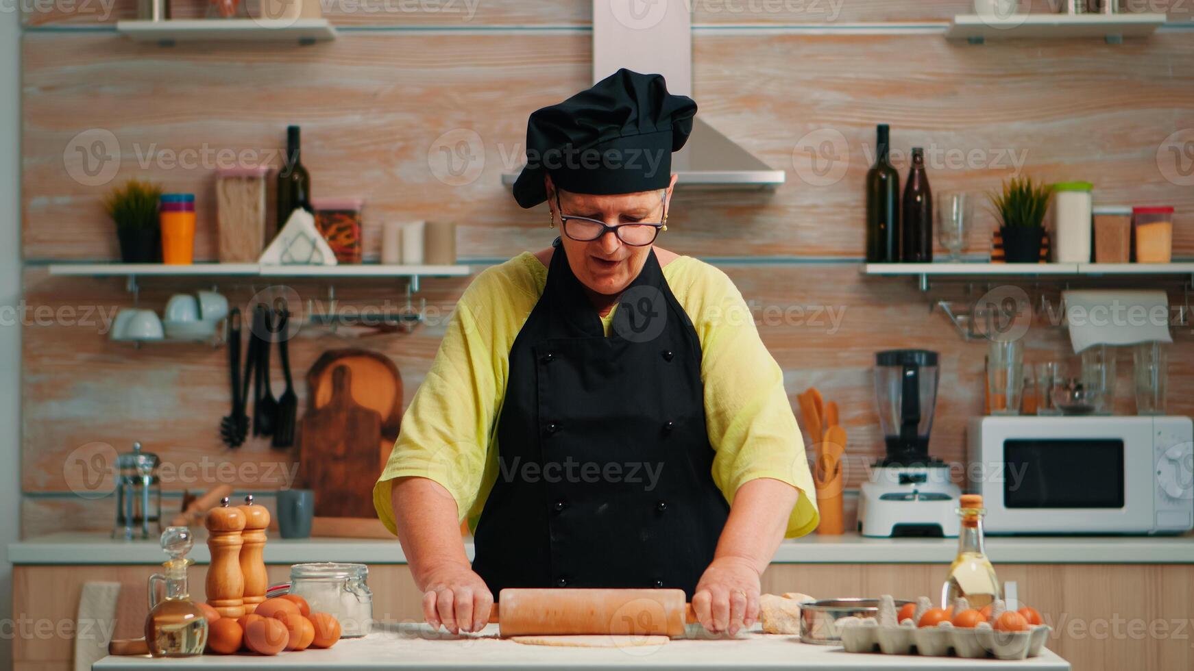 Baker woman rolling dough at home infront of video camera explaining recipe step by step. Retired blogger chef influencer using internet technology communicating on social media with digital equipment photo