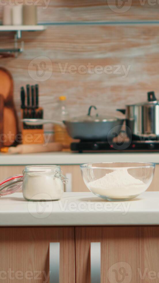 Pastry ingredients for homemade cakes and bread in empty kitchen. Modern dining room equipped with utensils ready for cooking with wheat flour in glass bowl and fresh eggs on table photo