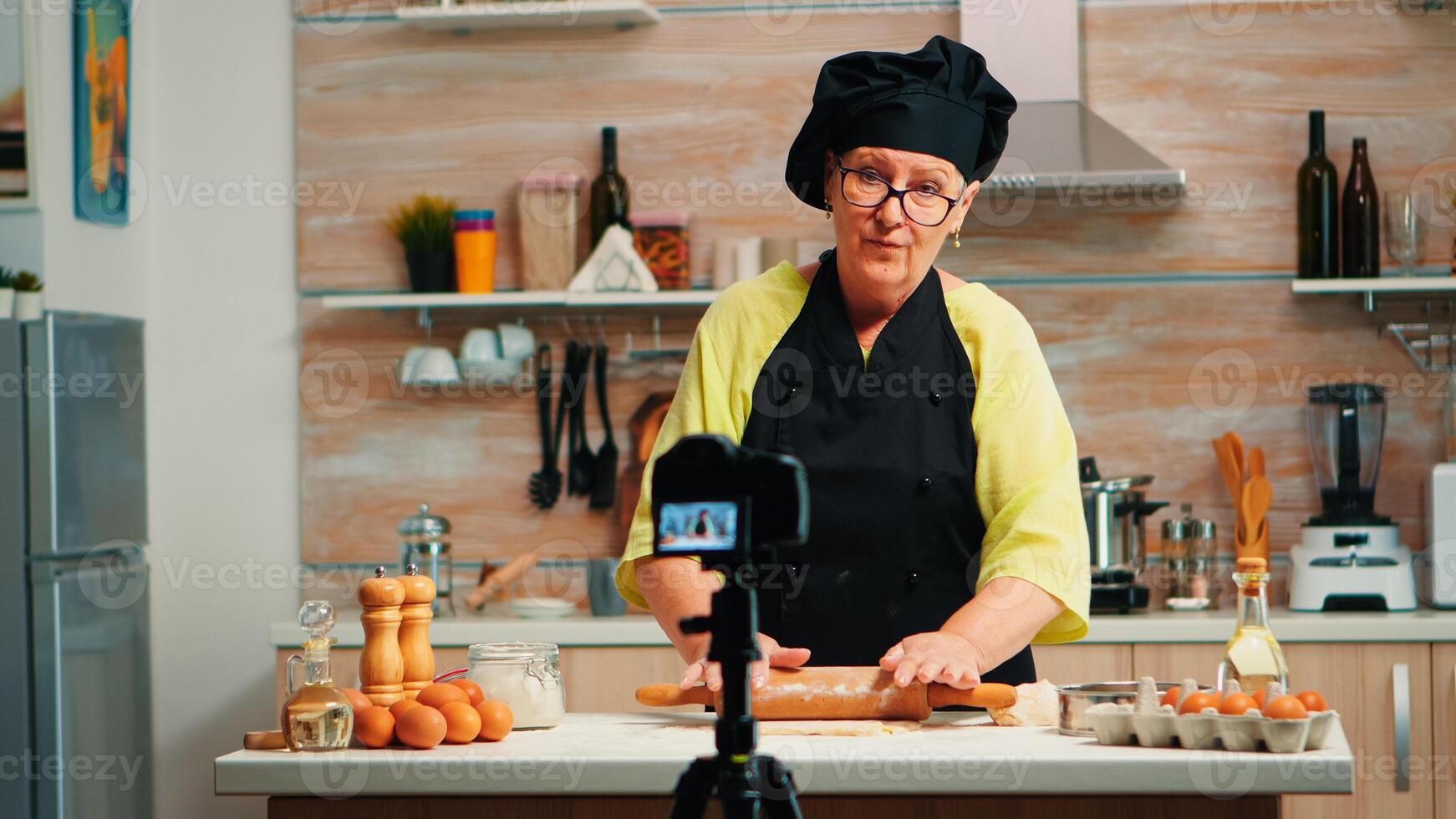 Grandmother making cooking vlog, recording herself on camera. Retired blogger chef influencer using internet technology communicating, shooting blogging on social media with digital equipment photo