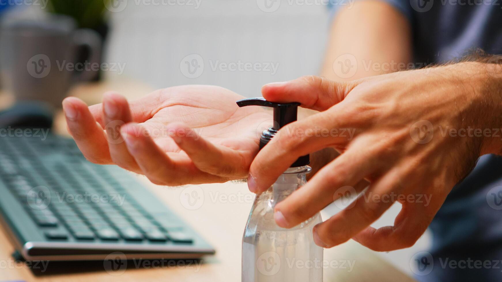 Close up of man using hand sanitizer sanitiser while working in office room. Entrepreneur in new normal company office workplace cleaning disinfecting hands using alcohol gel against corona virus. photo