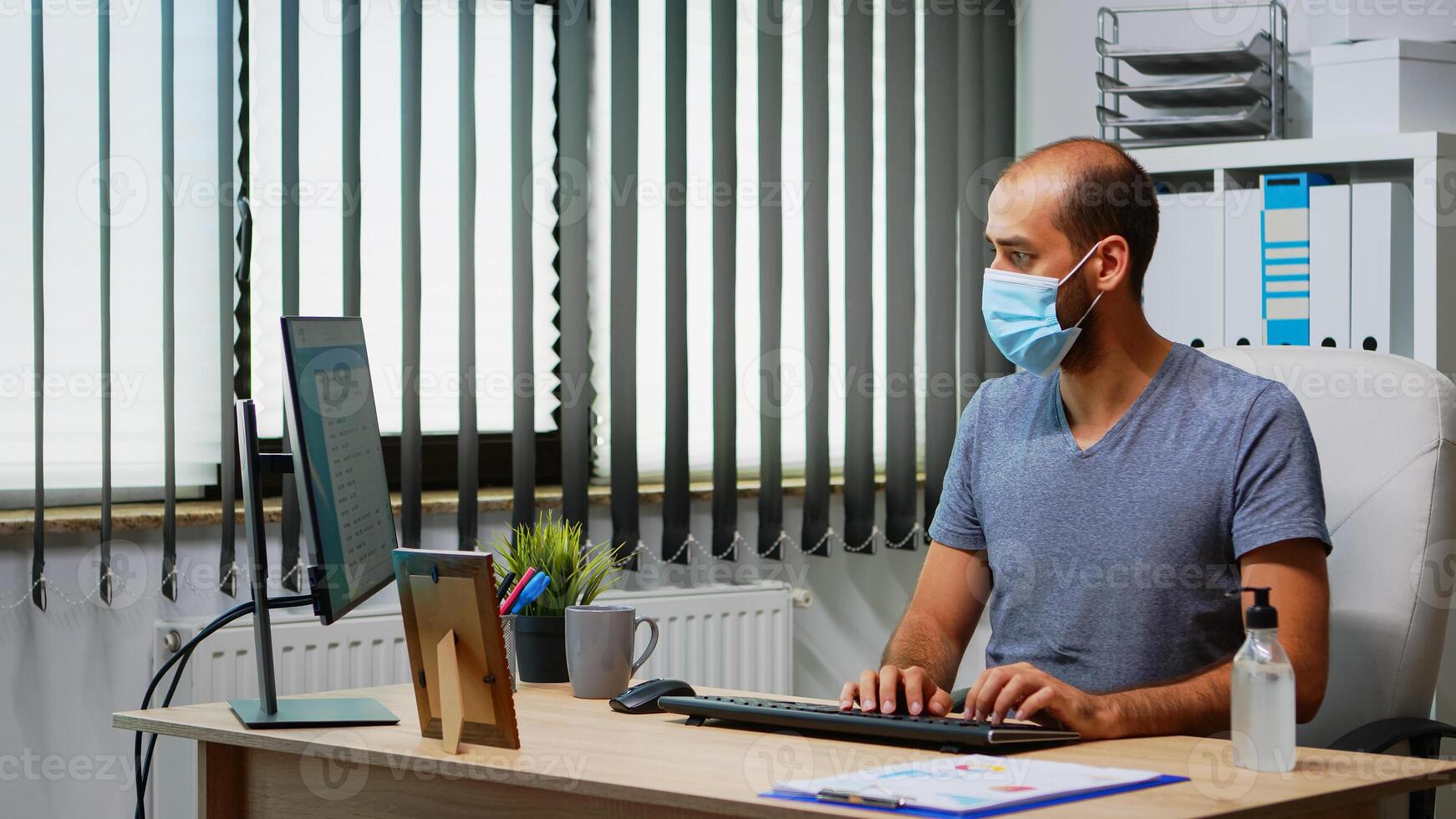 Employee with mask cleaning hands with antibacterian gel in office room before working at computer. Entrepreneur working in new normal office workplace using sanitize alcohol gel against corona virus photo