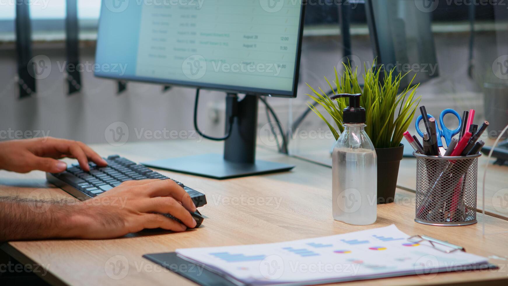 Close up of man using hand sanitizer alcohol gel in office with new normal before working at computer. Entrepreneur sitting in workplace cleaning disinfecting hands against corona virus. photo