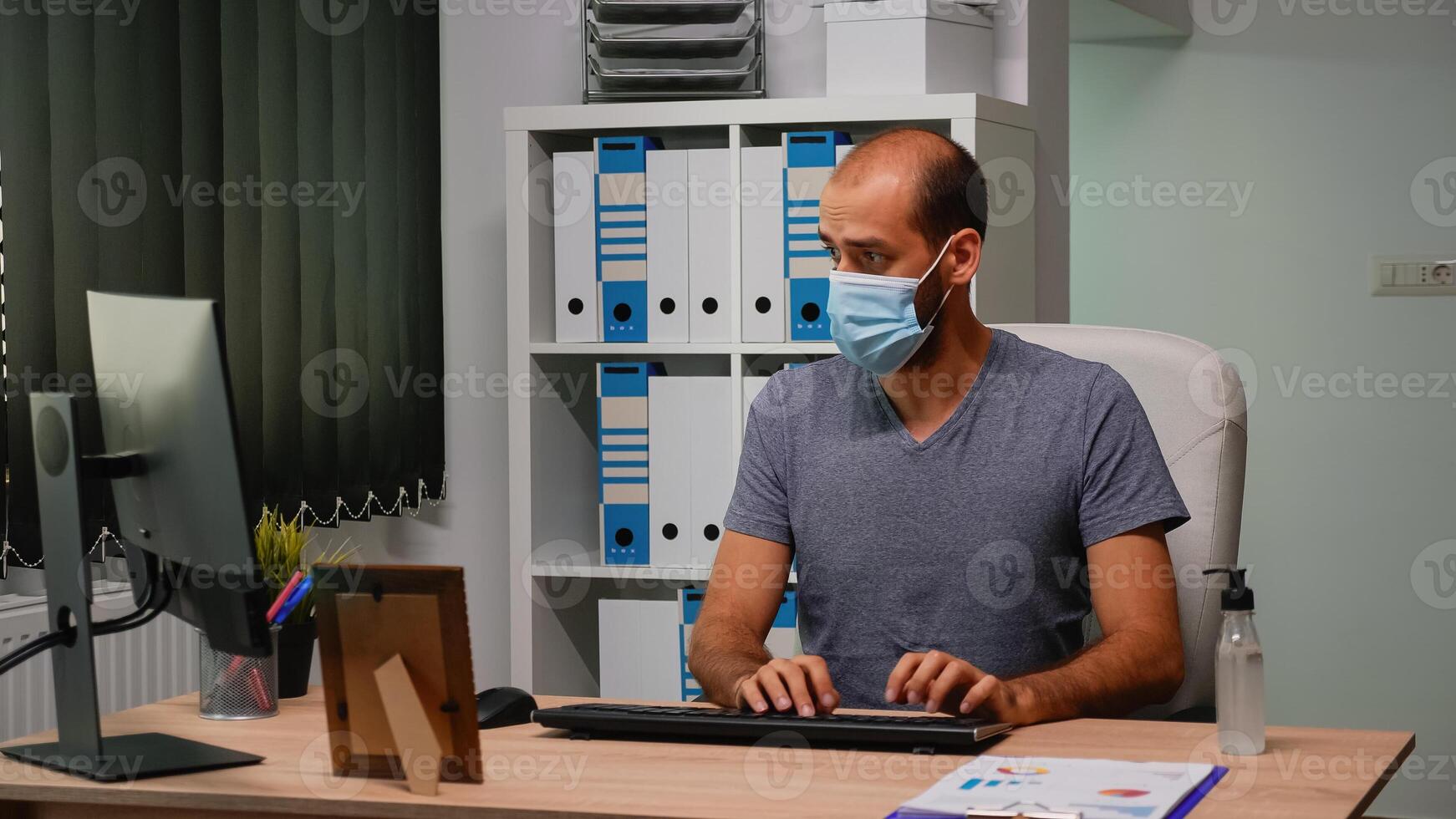 Entrepreneur with mask typing on computer sitting in new normal workplace. Freelancer working in modern office workspace cleaning hands using sanitize alcohol gel against corona virus photo