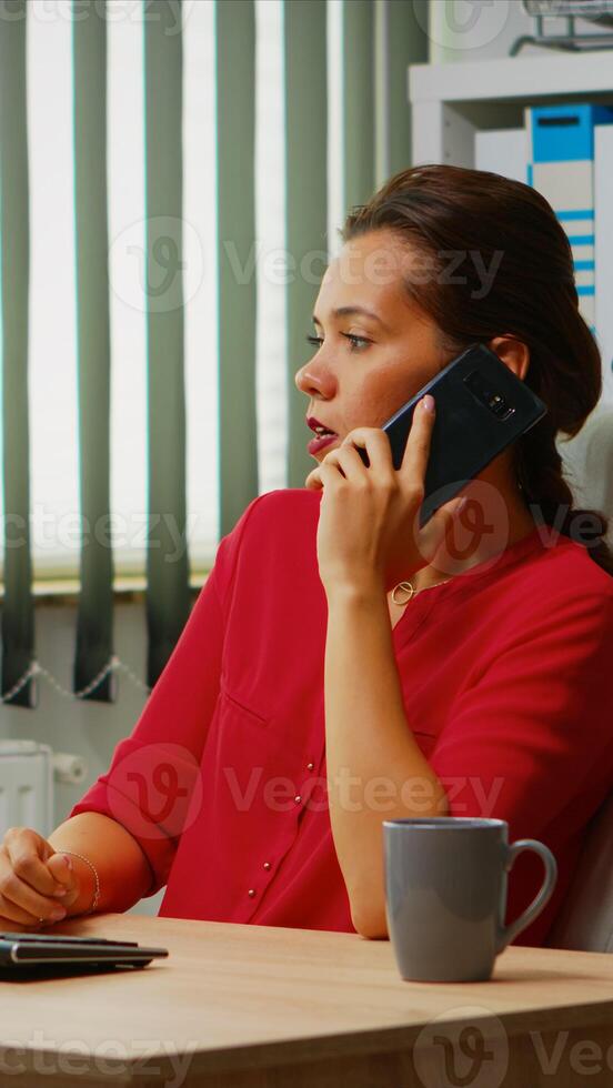 Employee talking on phone in business modern office. Hispanic entrepreneur working in professional workspace, workplace in personal corporate company speaking on smartphone looking at computer desktop photo