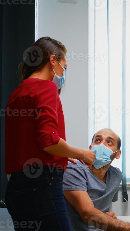 Colleagues with masks discussing graphics sitting in new normal office room. Coworkers talking working pointing at desktop respecting social distancing against covid virus using plexiglass. photo