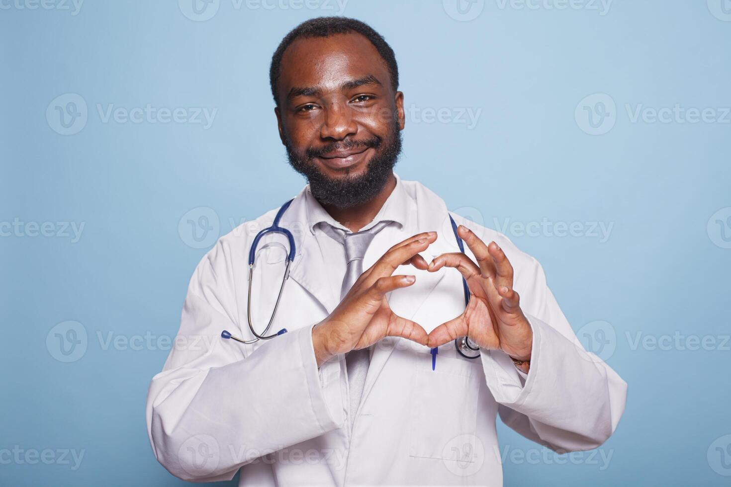 africano americano médico facultativo con un estetoscopio en pie terminado un aislado azul antecedentes sonriente y demostración un corazón símbolo con manos. romántico concepto. foto