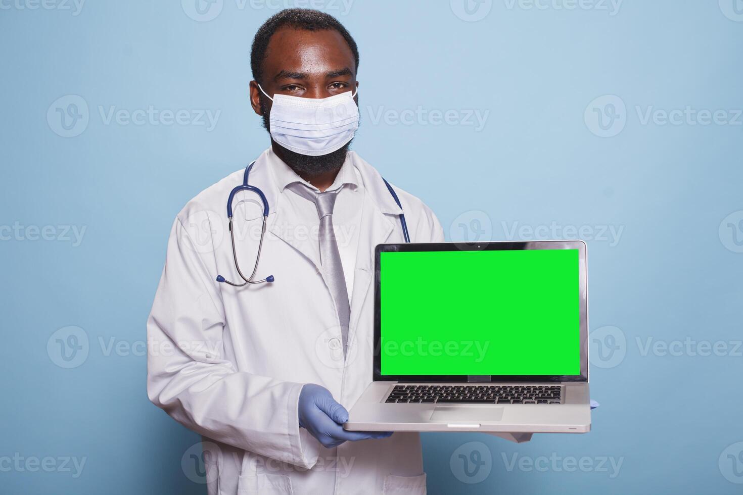 Physician wearing medical protective gear presenting laptop with green screen mockup for healthcare concept. African american doctor holding minicomputer displaying blank chromakey template. photo