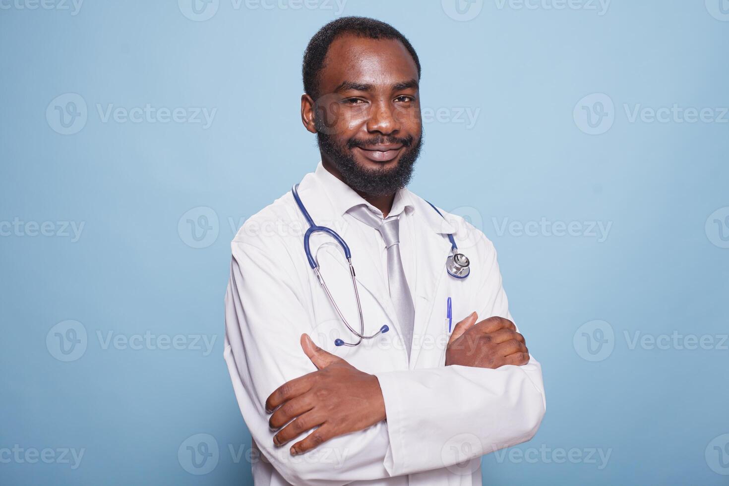 retrato de negro masculino médico con confianza posando con cruzado brazos para el cámara en estudio. africano americano médico especialista vistiendo laboratorio Saco es en pie en contra aislado fondo. foto