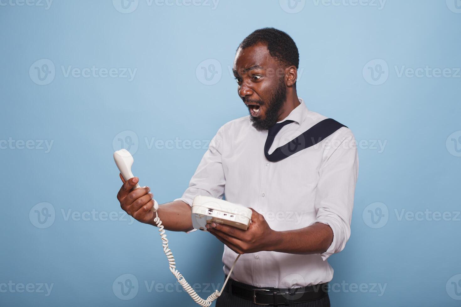 After losing an argument with person on other end of line, stunned businessman stares in awe at receiver of a cord phone. Office worker holding landline phone, cannot believe what he is hearing. photo