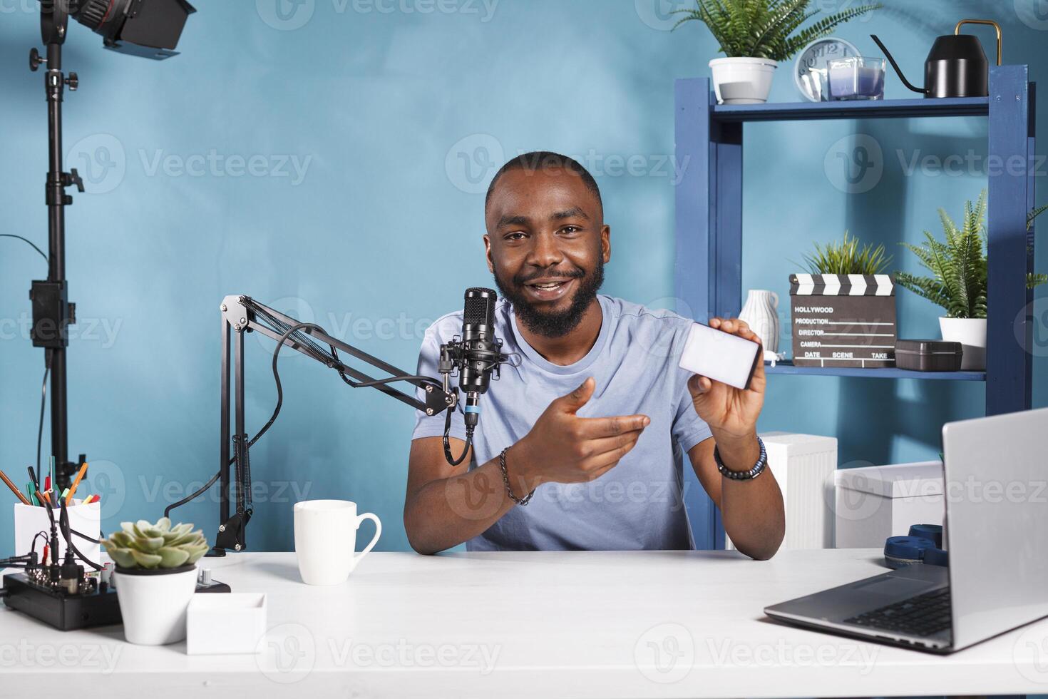 Blogger showcasing photography lighting equipment while recording product video review. Smiling african american man testing and recommending camera lamp for videography while streaming photo