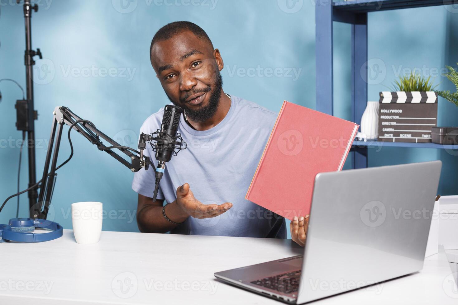 Smiling african american vlogger recording book presentation video and looking at camera. Young man streamer advertising and reviewing new novel while broadcasting for social network channel photo