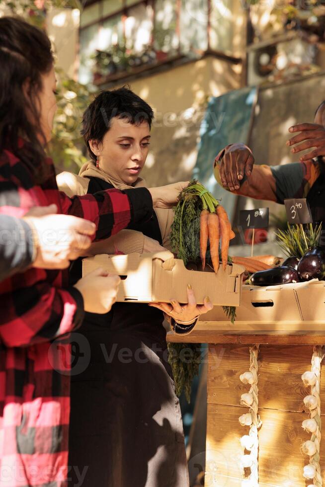 Team of vendors selling fresh fruits and veggies in boxes, serving elderly man and young woman at local farmers market. Smiling people looking at healthy organic colorful products. photo