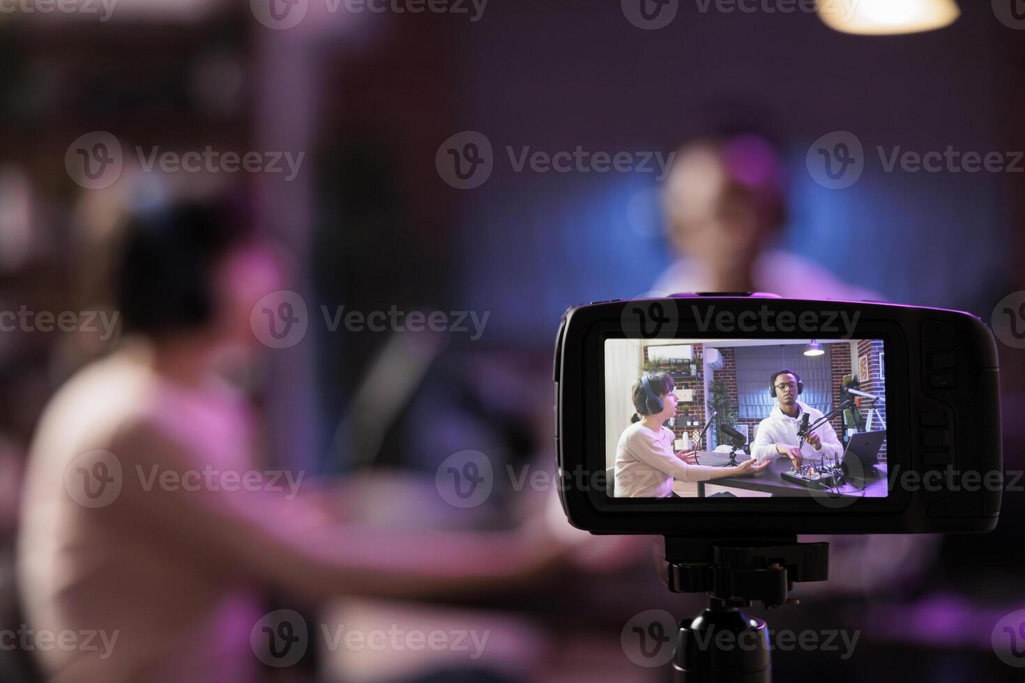 Close up shot of professional camera with podcast host and african american guest streaming online on live broadcast in blurry background. Professional recording tools in living room studio photo