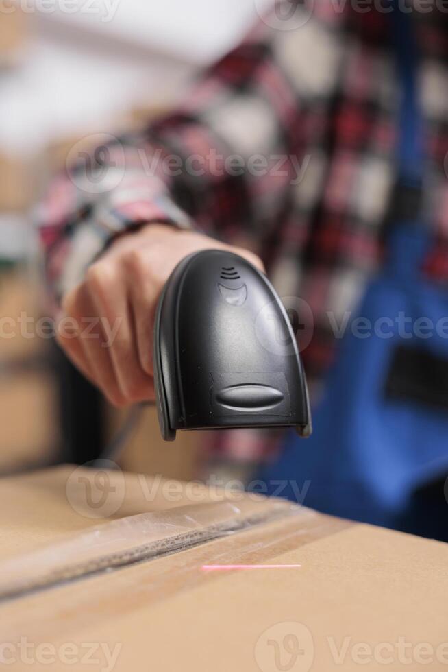 Delivery service employee scanning parcel and managing packages storing in warehouse. Storehouse worker doing shipment operations while holding barcode scanner in hand close up photo