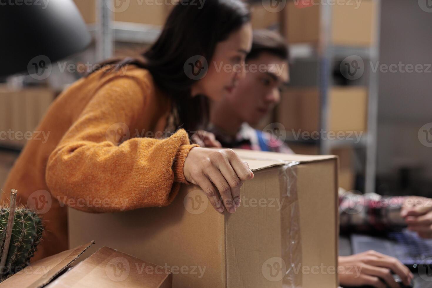 Warehouse employees holding packed package and creating invoice on laptop. Storehouse asian coworkers checking pick ticket on computer and managing parcel sending in storage room photo