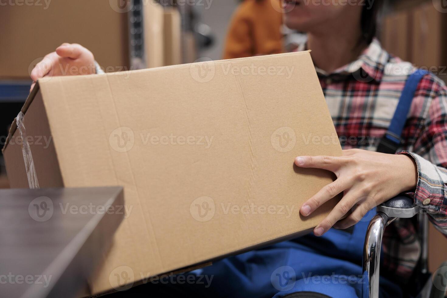 Postal service worker with disability holding package while working in warehouse. Shipment company storehouse employee managing parcles delivery and preparing cardboard box photo
