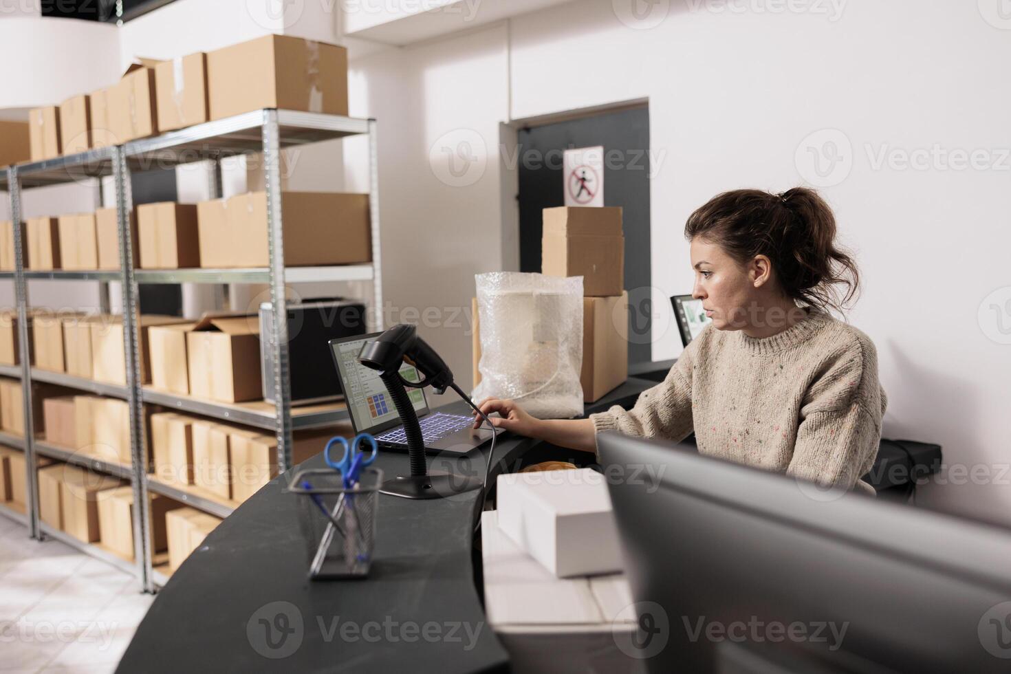 Storage room manager standing at counter desk, analyzing merchandise logistics report on computer. Stockroom employee checking customers online orders preparing packages for shipping in storehouse photo