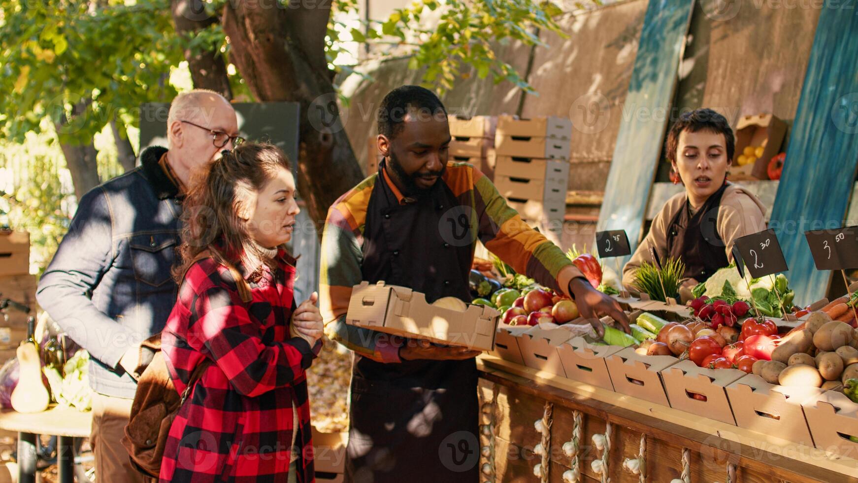 African american farmer putting fresh products in box, selling package of natural bio fruits and vegetables. Young woman talking to local marketplace vendor, buying organic produce. photo