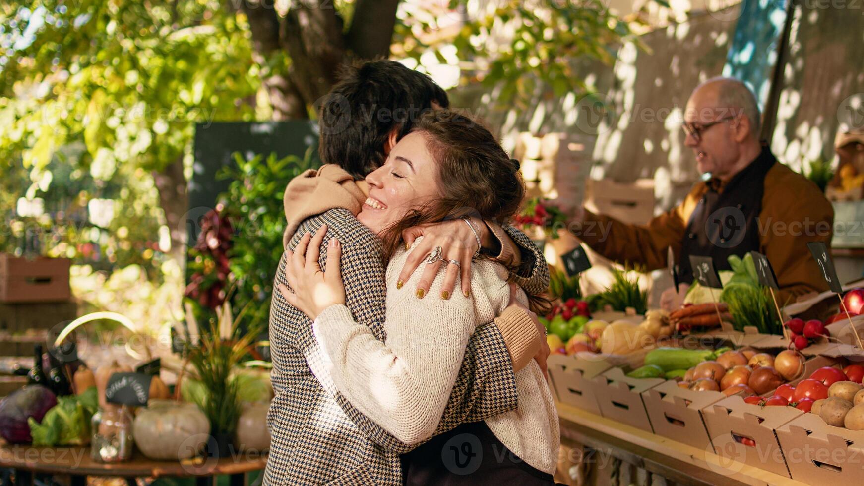 Woman vendor greeting regular client and hugging at farmers market stand, being happy selling locally grown products. Positive farmer sharing hug with customer, enjoying visit at street festival. photo