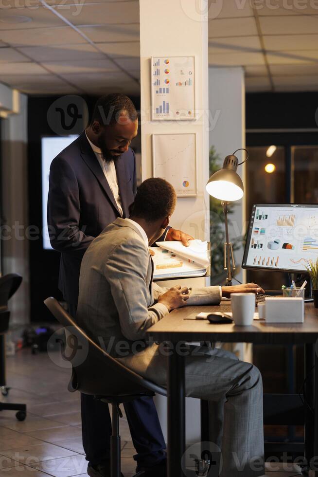 Employees looking at financial statistics on computer, discussing financial strategy in startup office. Businessman with manager working over hours investment plan. Business concept photo