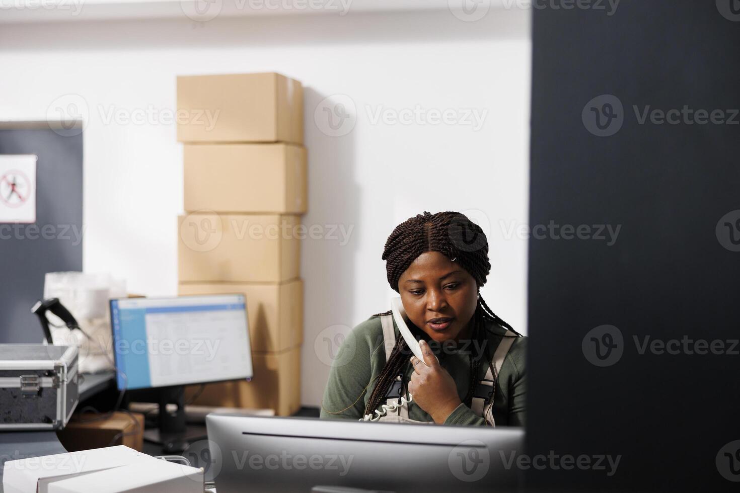 Storage room employee having remote discussion with customer during storehouse inventory. African american supervisor analyzing merchandise logistics on computer, preparing client order photo